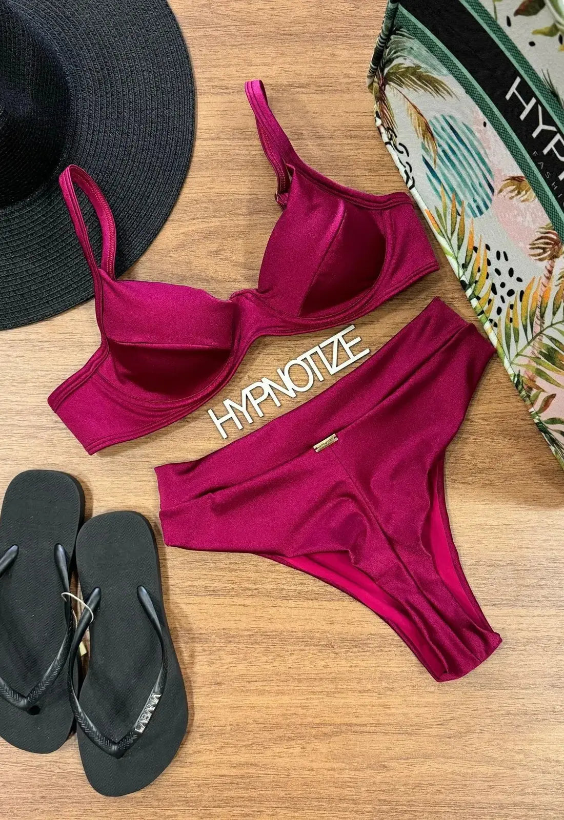 Bikini burdeos con top de aro y braguita alta, junto a accesorios de playa.